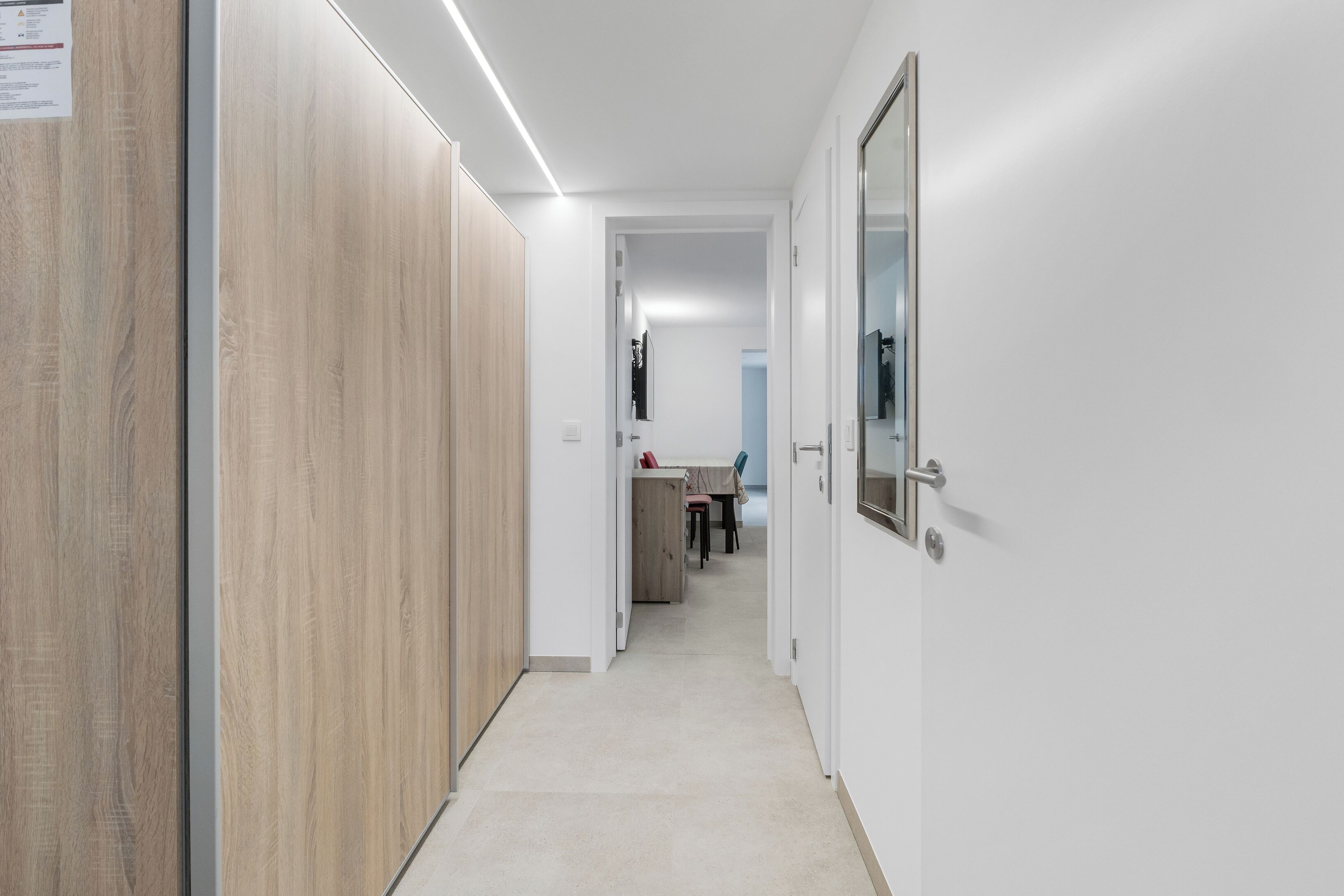 A hallway with wooden paneling, a tiled floor, and a door with a mirror.