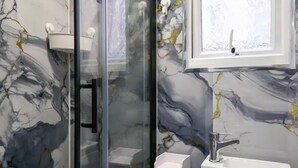 A bathroom with a glass shower enclosure, a white sink, and a marble-patterned wall.