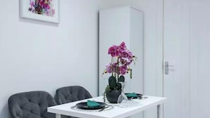 A dining area with a white table, two grey chairs, a vase with purple flowers, and a cabinet in the background.