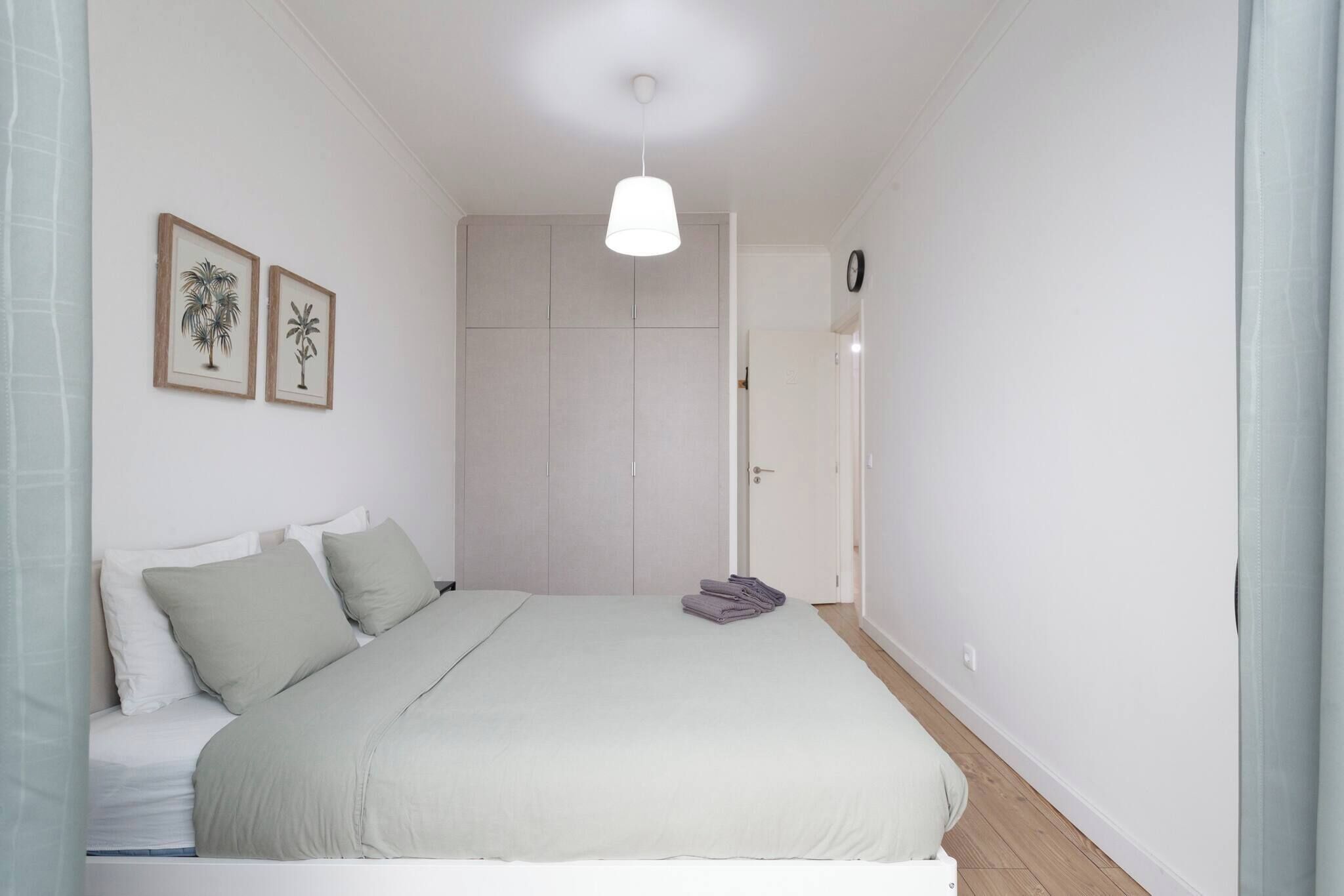 Une chambre à coucher avec un lit, des oreillers, un luminaire suspendu et une porte donnant sur une autre pièce.
