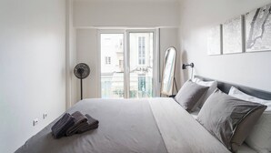A bedroom with a bed, a standing fan, a clock, and cityscape artwork on the wall. - Charming 2-bedroom Apartment in Almada, Near Lisbon (Almada)