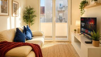 A living room with a sofa, a TV, a plant, and a view of the outside.