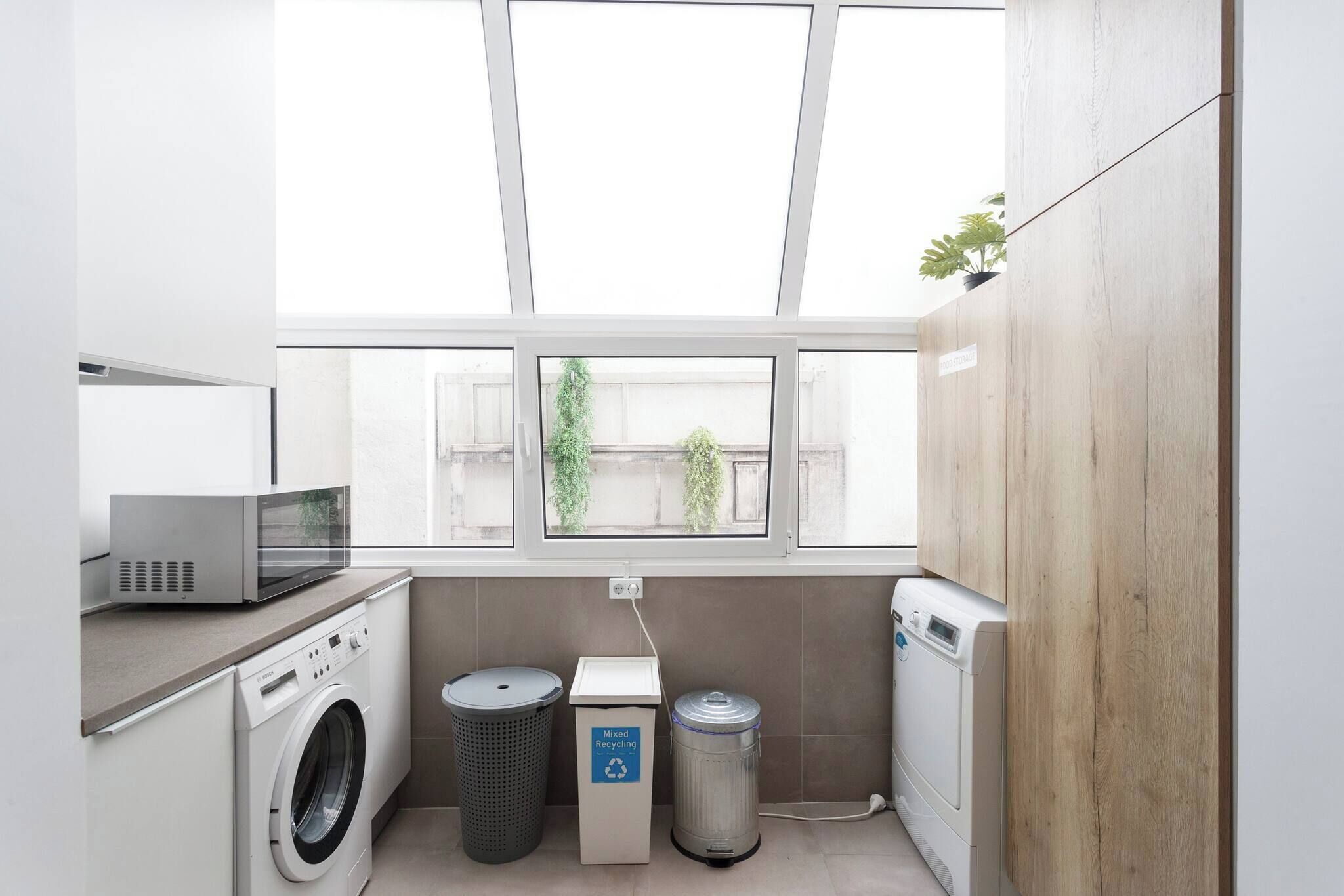 Una sala de lavandería con lavadora, secadora, microondas y contenedores para reciclaje.