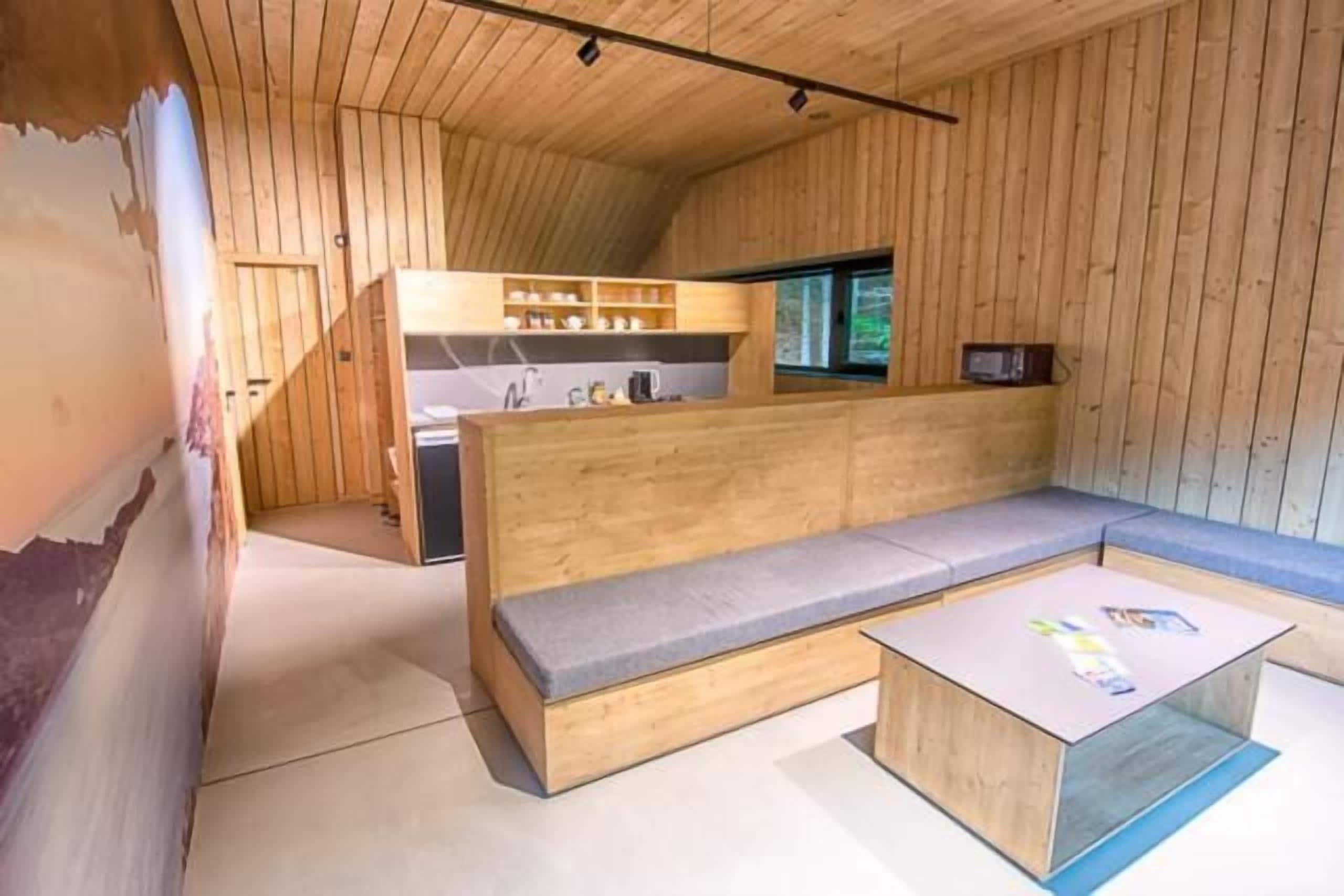 A modern interior with a wooden bench, a small kitchen area, and a window.
