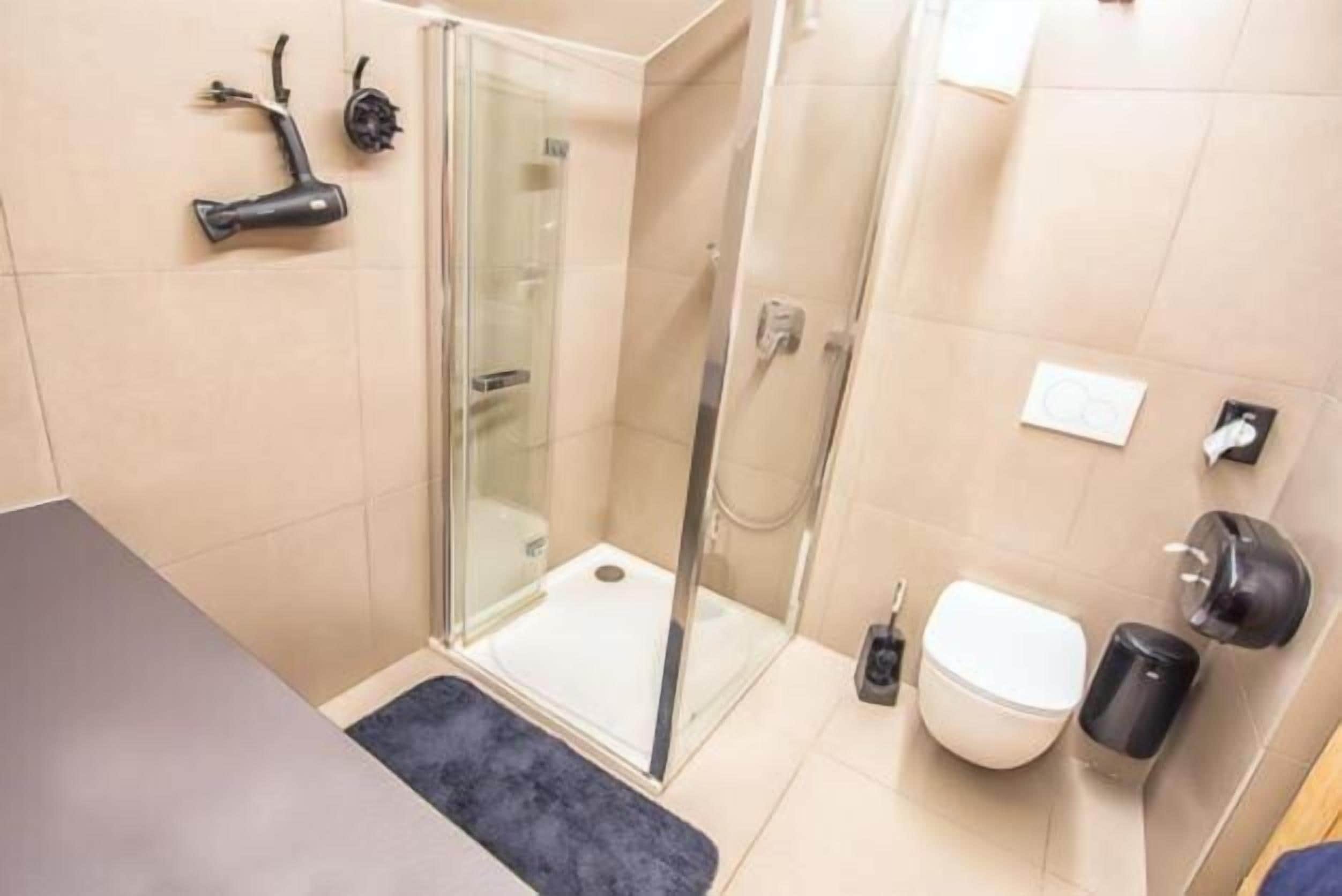 A bathroom with a glass shower enclosure, a toilet, and a sink.