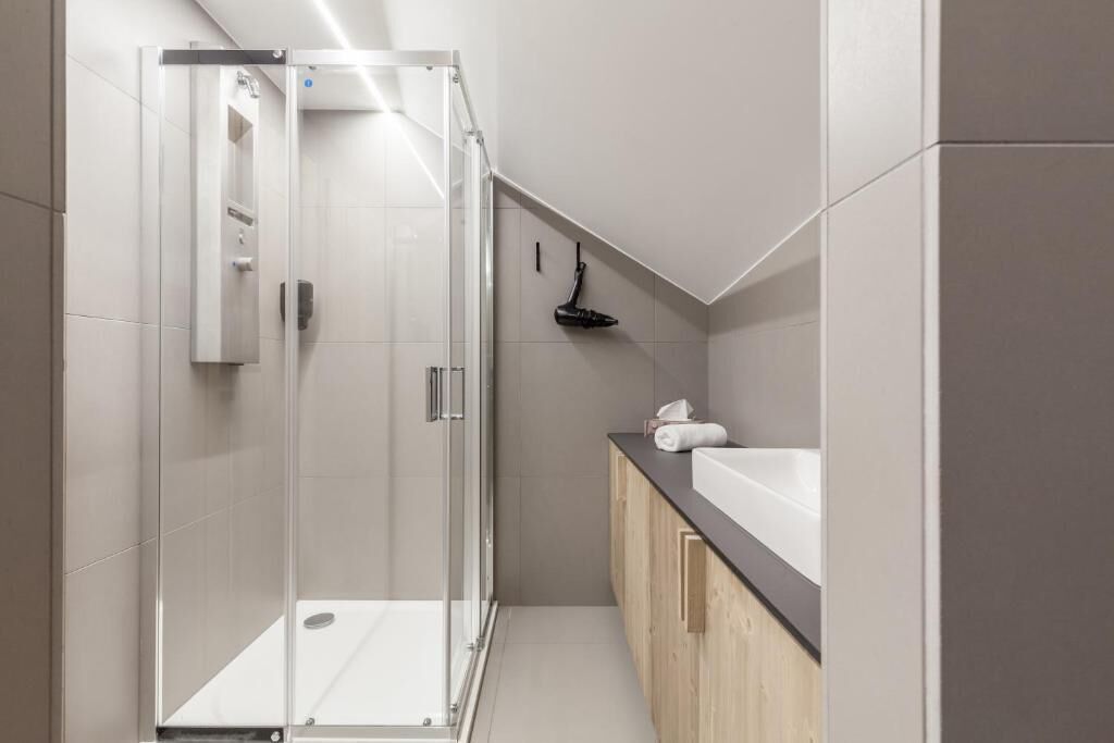 Un baño moderno con cabina de ducha de vidrio, un lavabo blanco y armarios de madera.