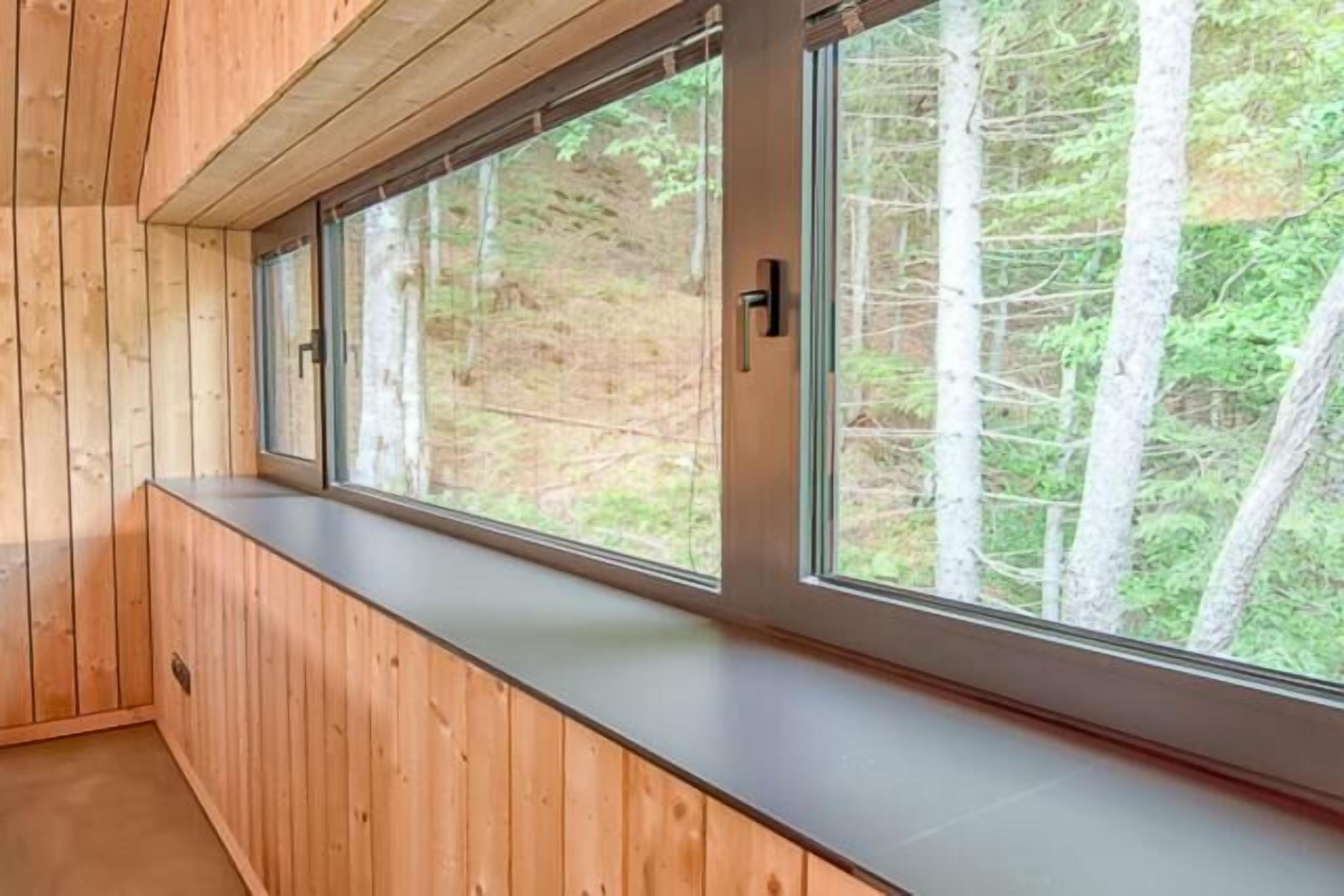 A room with a wooden bench along a window with a view of trees.