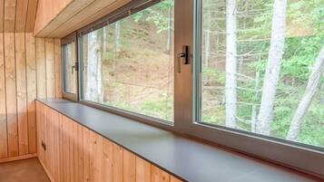 A room with a wooden bench along a window with a view of trees.