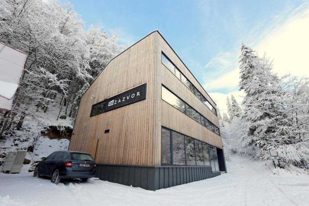Un edificio moderno de dos pisos con fachada de madera y grandes ventanales, rodeado de árboles cubiertos de nieve.
