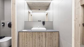 A modern bathroom with a wooden vanity, a white sink, and a mirror above it.