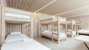 A room with bunk beds and a table, wooden walls, and a ceiling with linear lights. - Chata Zázvor (HORNÁ LEHOTA)