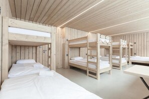 Una habitación con literas y una mesa, paredes de madera y un techo con luces lineales.