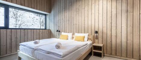 A wooden-paneled bedroom with a large bed, bedside tables, and a window with a view of trees.