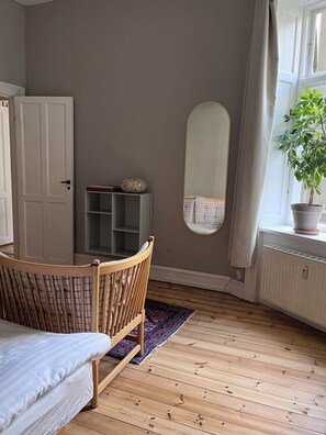 Une pièce comprenant un lit, une chaise en bois, un miroir, une plante en pot et un radiateur.