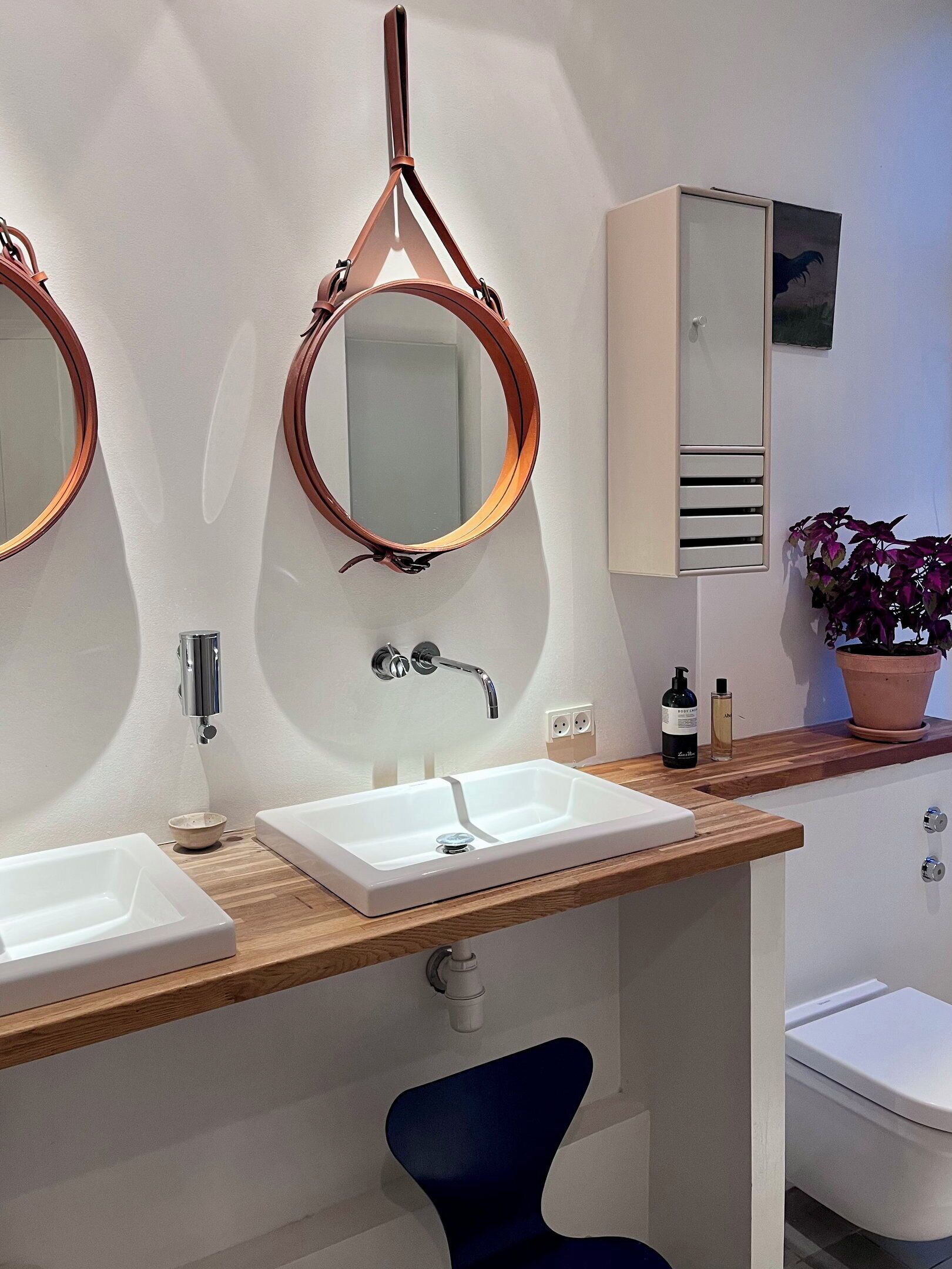 A modern bathroom with two sinks, a mirror, a cabinet, and a toilet.