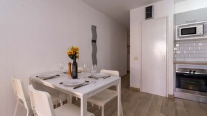 A dining area with a white table set for four, a vase with yellow flowers, and a modern kitchen with a microwave and oven. - Castle Harbour 4 - 1-Bedroom Apartment (Los Cristianos)