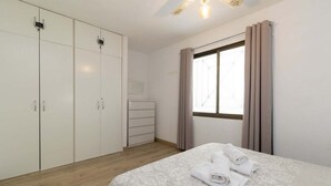 A bedroom with a bed, a wardrobe, a dresser, and a window with curtains. - Castle Harbour 4 - 1-Bedroom Apartment (Los Cristianos)