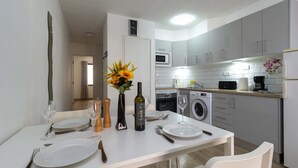 A modern kitchen with white cabinets, a dining table set with plates, wine glasses, and a bottle. - Castle Harbour 4 - 1-Bedroom Apartment (Los Cristianos)