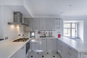 Una cocina moderna con armarios blancos, una estufa a gas, una campana extractora de acero inoxidable y una ventana con persianas.