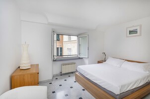 Un dormitorio con cama, mesita de noche, lámpara, ventana y radiador.