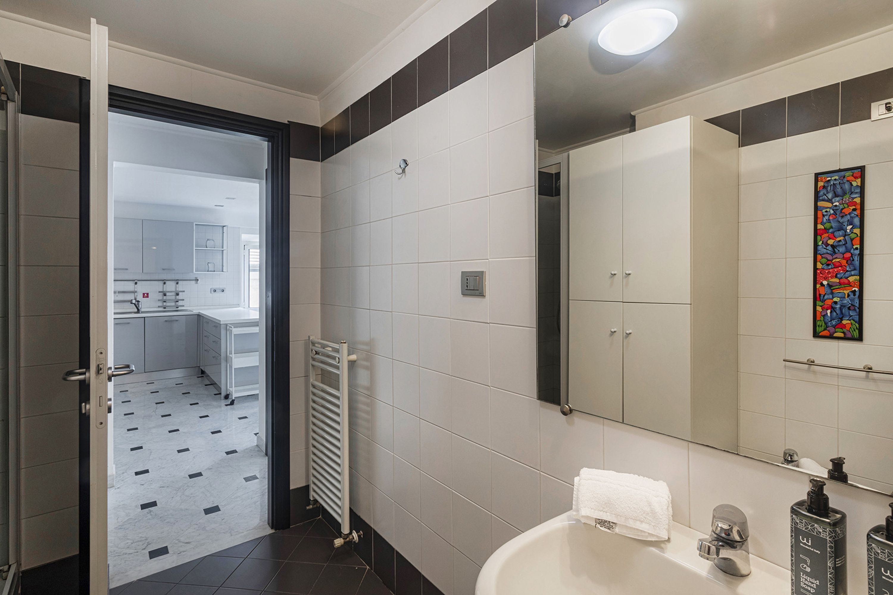 A modern bathroom with a white bathtub, a large mirror, and a colorful artwork on the wall.