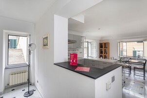 Una cocina moderna con una isla central, un comedor con mesa y sillas, y vistas al exterior a través de una ventana.