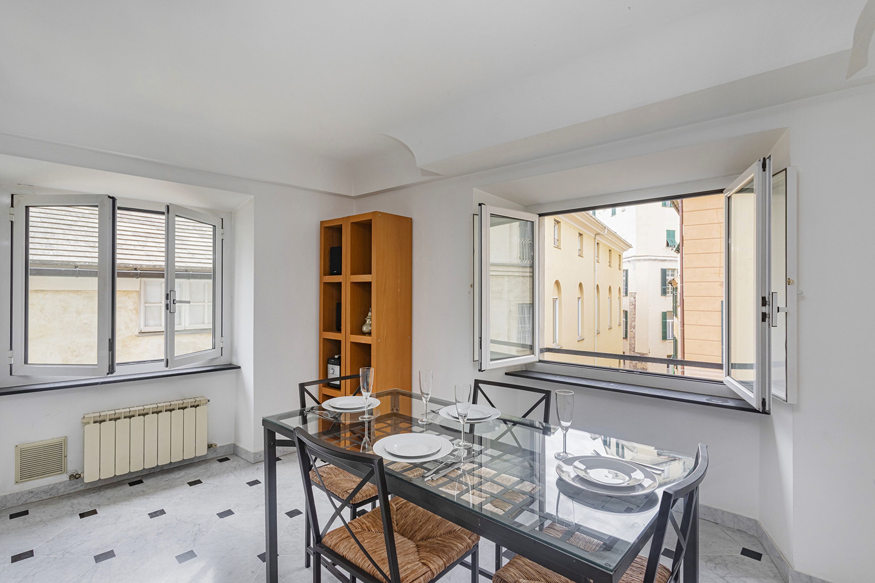 A dining area with a glass table, chairs, and a wooden bookshelf.