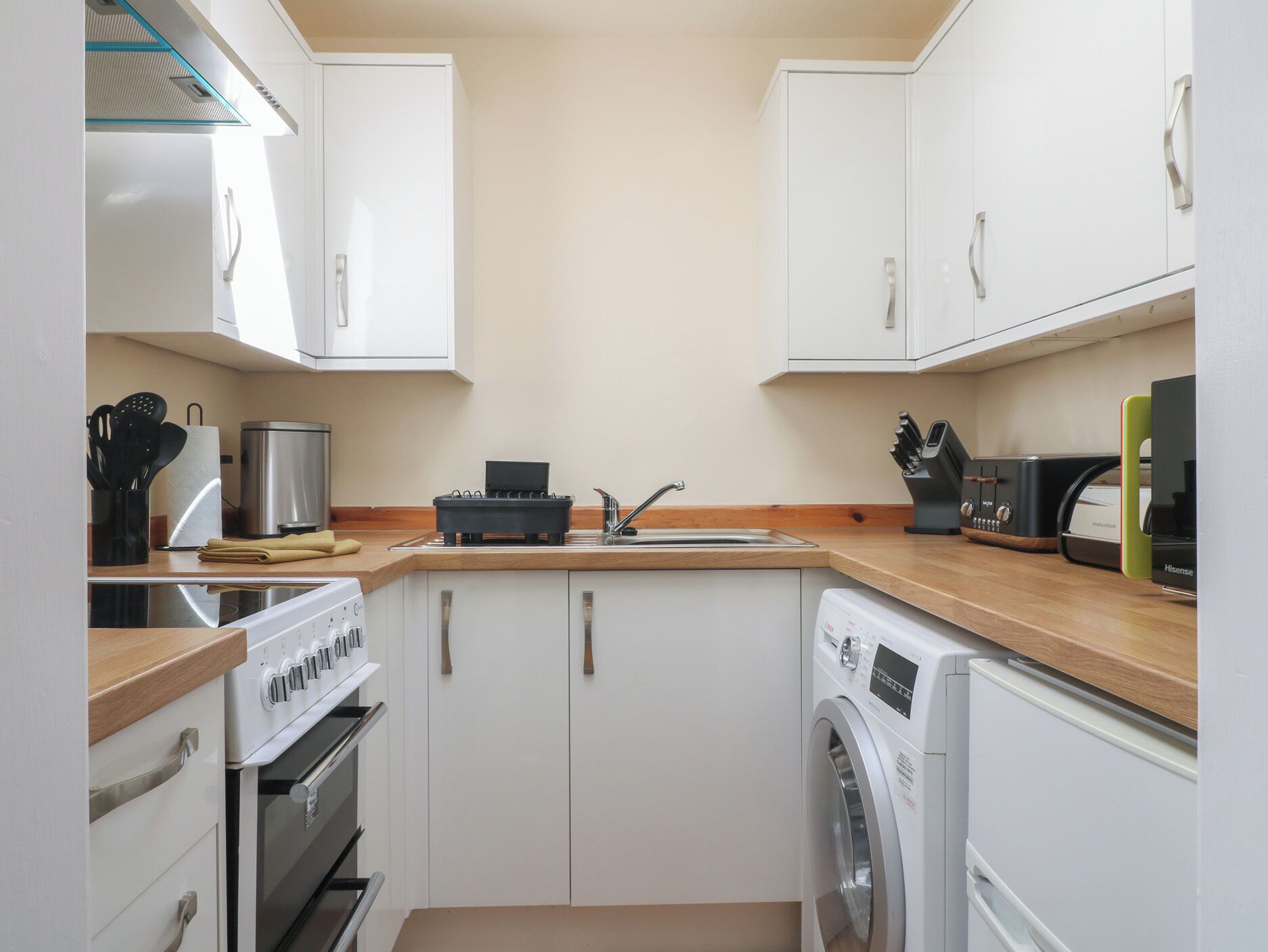 A compact kitchen with white cabinets, a sink, a stove, a microwave, and a washing machine.