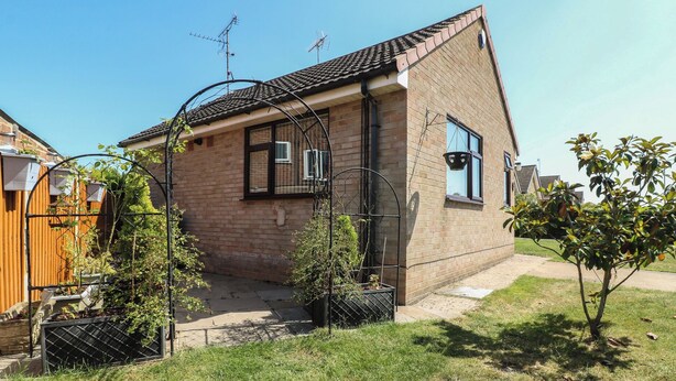 Una casa de ladrillo con techo de tejas, un pequeño jardín y una cerca de metal.