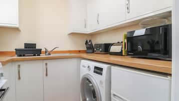 A compact kitchen with a washing machine, microwave, toaster, and cabinets.