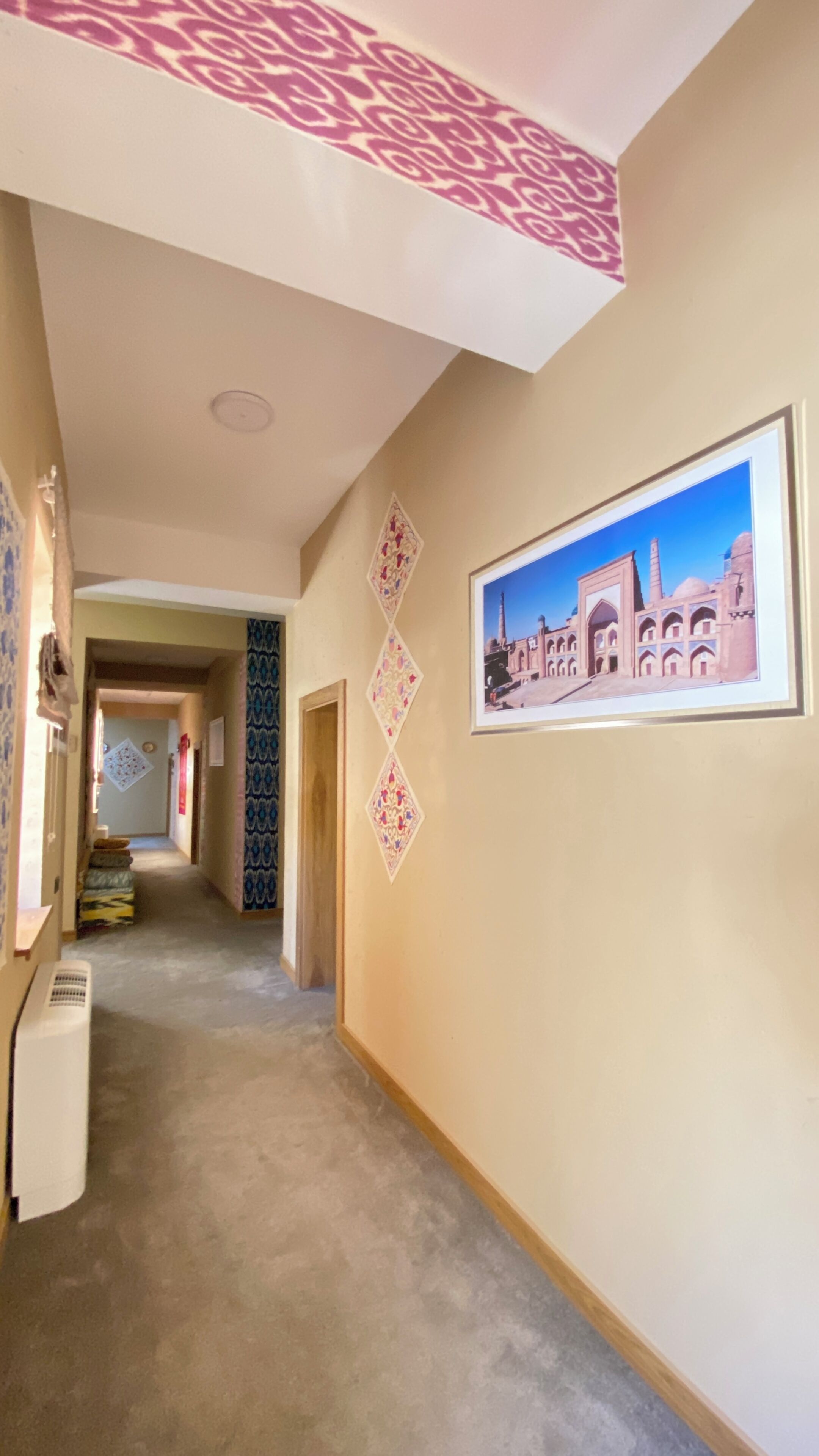 A hallway with patterned wallpaper, a framed picture of a building, and a radiator.