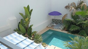 Ein Poolbereich mit Liegestühlen, einer kleinen Sitzecke mit Kissen und verschiedenen Pflanzen.