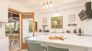 Een moderne keuken met een groot kookeiland, houten stoelen, een eethoek en uitzicht op groen.