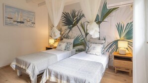 Een slaapkamer met twee bedden, een hemelbed, een nachtkastje met een lamp, een schilderij aan de muur en een potplant.