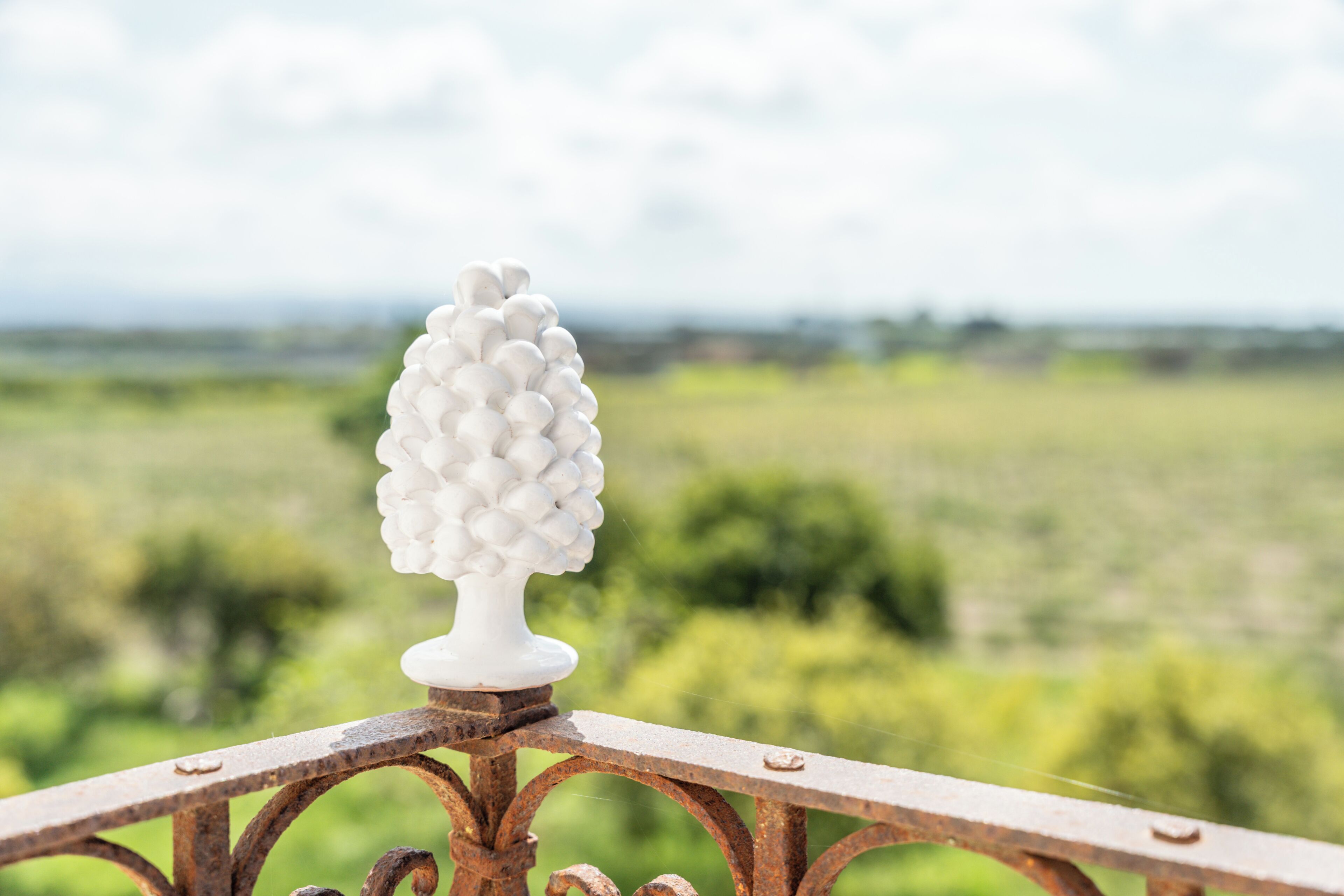 A white decorative object on a metal railing with a blurred green landscape in the background.