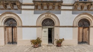 Un edificio con una puerta central, dos plantas en macetas y un área de entrada con baldosas.