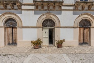 Un edificio con una puerta central, dos plantas en macetas y un área de entrada con baldosas.