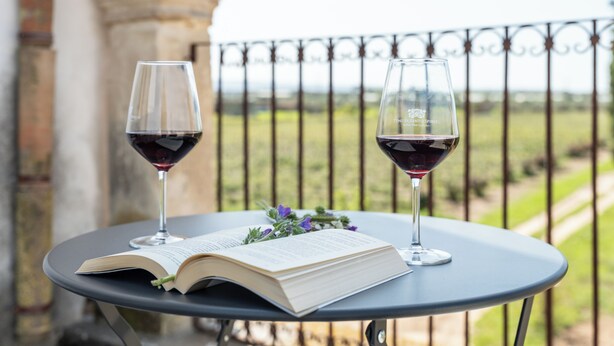 Una mesa con un libro abierto y dos copas de vino en un balcón.