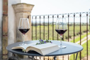 Una mesa con un libro abierto y dos copas de vino en un balcón.
