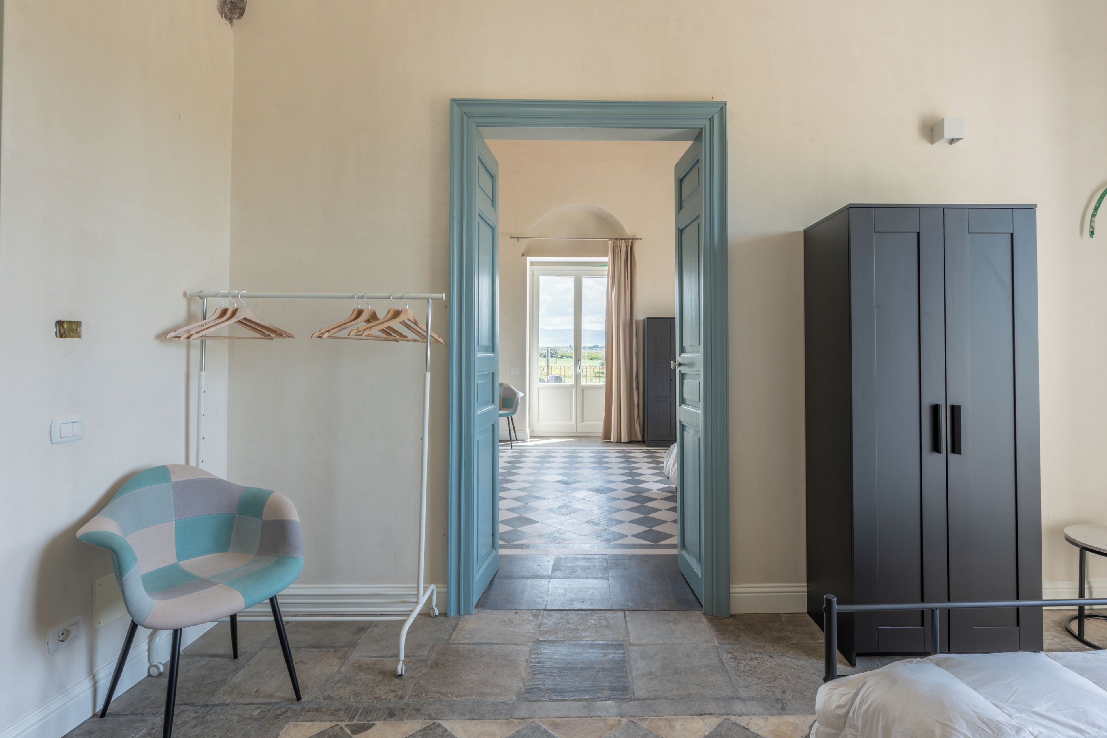 Ein Zimmer mit Bett, Kleiderschrank, Stuhl und einem zur anderen Kammer führenden Gang.
