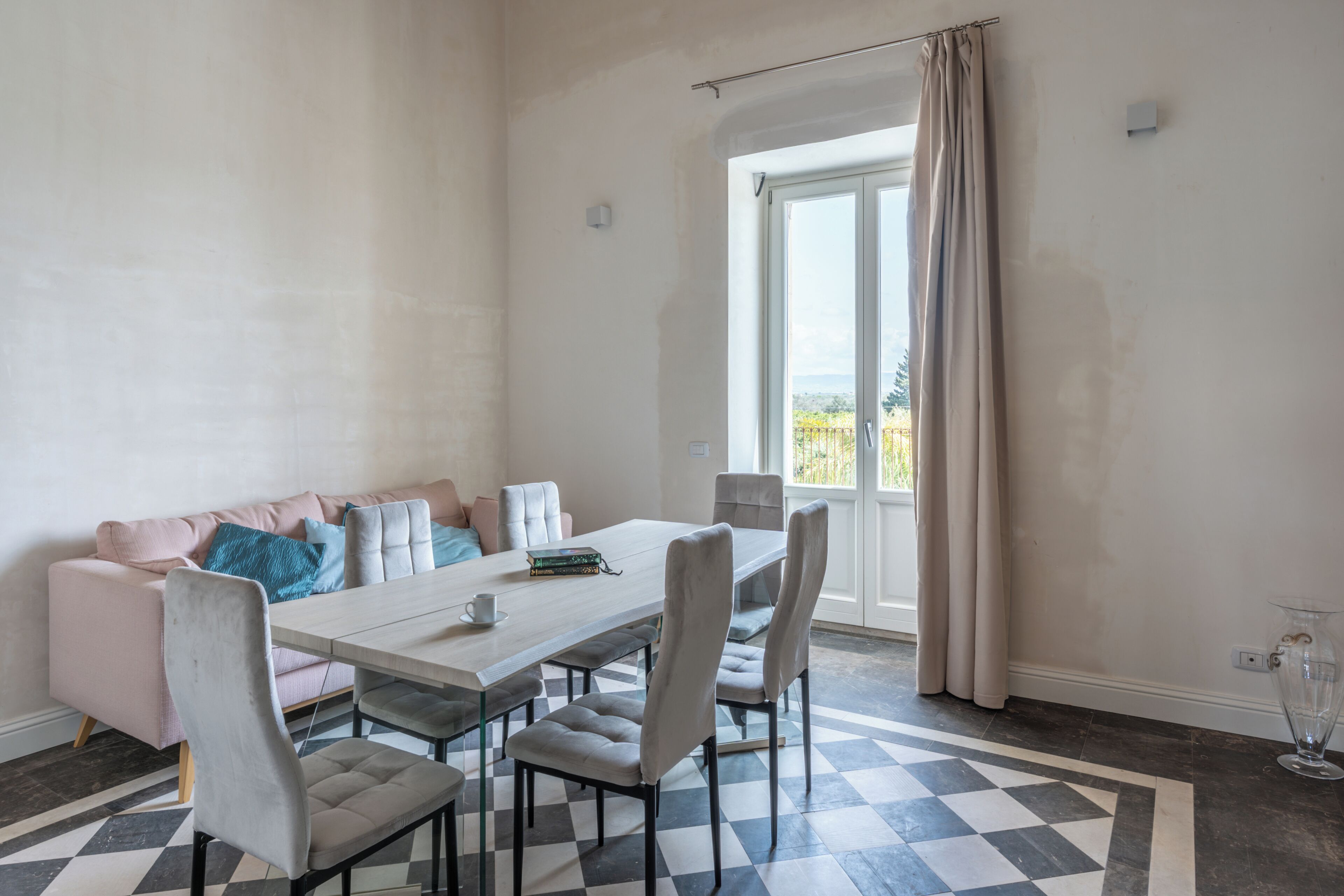 A dining area with a table, chairs, a sofa, and a view through a window.