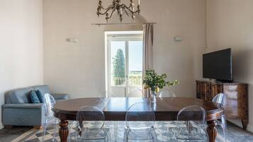 A dining area with a wooden table, clear chairs, a chandelier, a television, and a sofa.