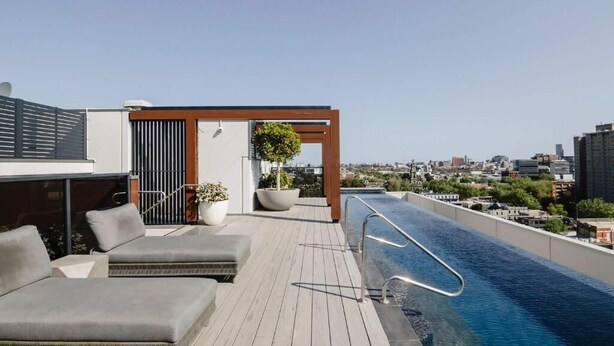 A rooftop pool area with lounge chairs, a wooden pergola, and a city view. - 101-251 Johnston St (Abbotsford)