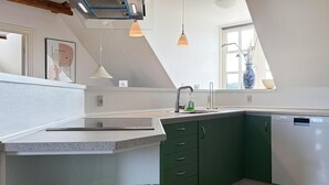 Une cuisine moderne dotée d’un lave-vaisselle encastré, de meubles de couleur verte et d’un éclairage suspendu.