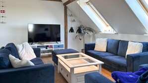 Un salon moderne avec un téléviseur, des canapés, une table basse et une lucarne.