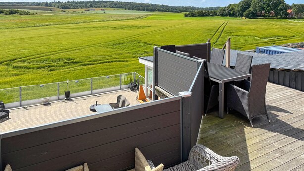 Une terrasse sur le toit, aménagée avec du mobilier d’extérieur, un barbecue et offrant une vue sur un champ verdoyant.