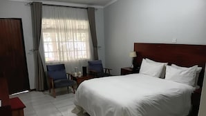 A hotel room with a large bed, two chairs, a nightstand, and a window with curtains.