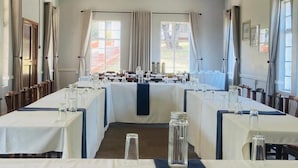 A dining area with tables set for service, large windows with curtains, and a view of the outdoors.