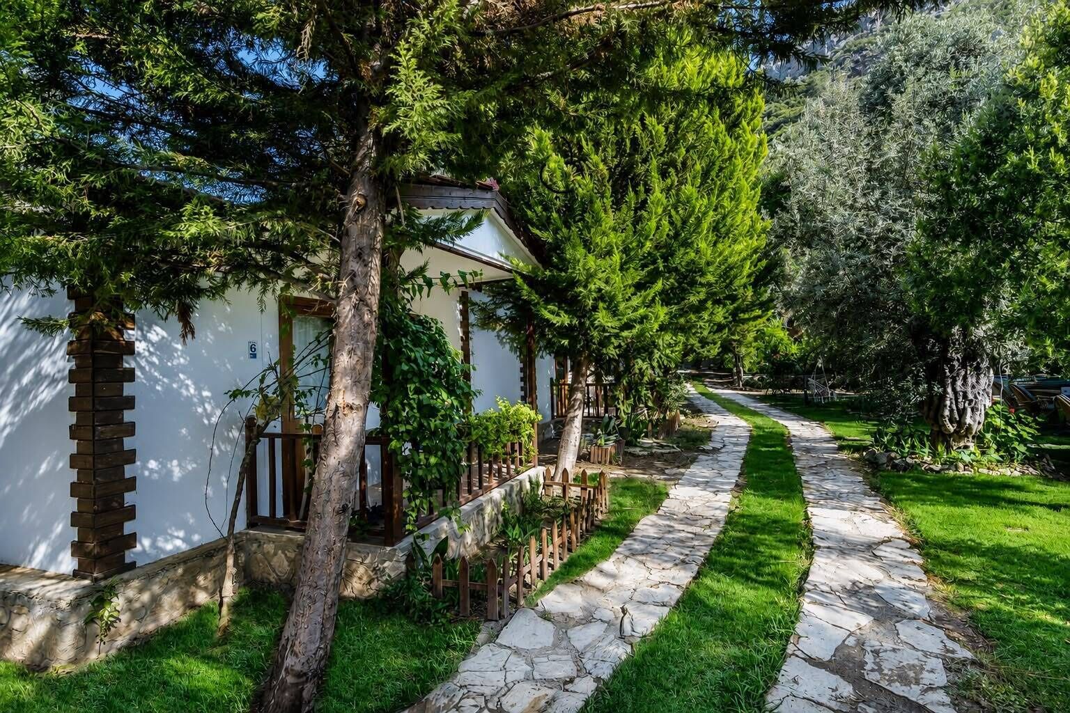 A stone pathway leading to a white building with a wooden fence and trees.