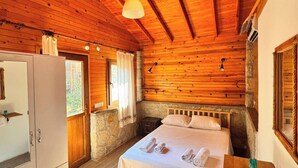 A wooden cabin room with a bed, a dresser, and a stone wall. - Petrinos Butik Otel (Datça)